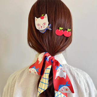Person with hair styled using cat and apple themed hair accessories and a matching scarf.