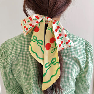 Person wearing a colorful hair scarf with cherry and bow pattern on a plain background