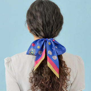 Person with a colorful hair scarf tied in a ponytail against a light blue background