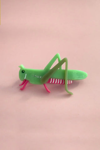 Green grasshopper hairclip on a pink background