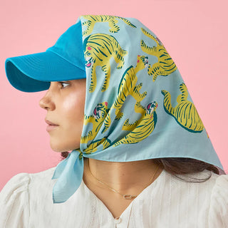 Person wearing a blue cap and a light blue headscarf with yellow tiger patterns on a pink background
