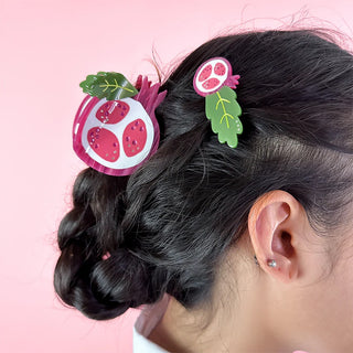 Person wearing hair accessories with pomegranate designs on a pink background