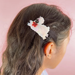 Hair clip with sheep design in a person's hair against a pink background