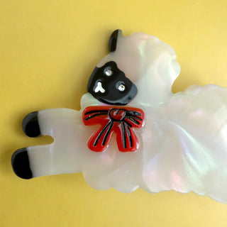 Sheep-shaped hair clip with a red bow on a yellow background