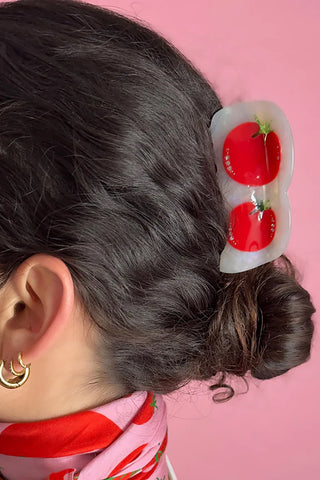Person with a bun wearing a hair clip with tomatoes design against a pink background