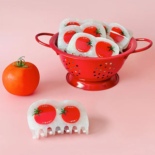 Red colander with tomato-themed hair clips on a pink background