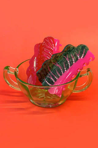 Pink and green chard shaped hair clips in a clear glass bowl on an orange background
