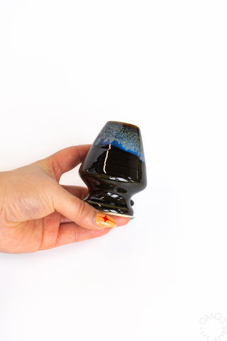 Hand holding a black ceramic whisk stand on a white background