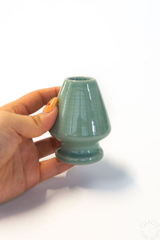 Hand holding a small green ceramic vase against a white background