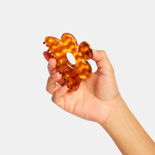 Hand holding a orange and honey checkered hair clip against a light gray background