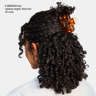Person with 3C curly hair styled with an amber hair clip on a white background