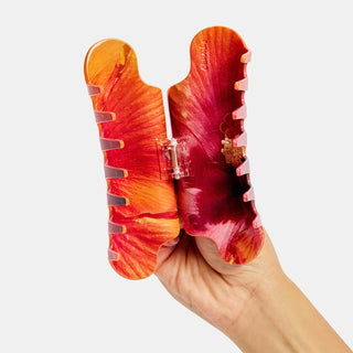 Hand holding red hibiscus patterned hair clip against a white background
