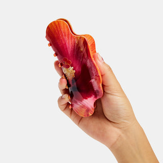 Hand holding a red and orange claw hair clip against a white background