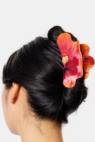 Person with dark hair wearing a red claw clip with a hibiscus print