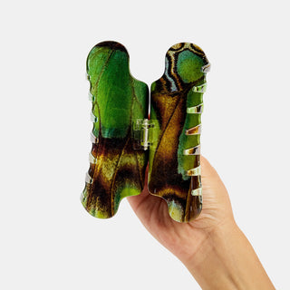 Hand holding a green and brown claw hair clip opened against a white background