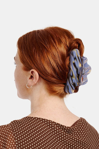 Person with red hair using a blue and black claw hair clip against a white background