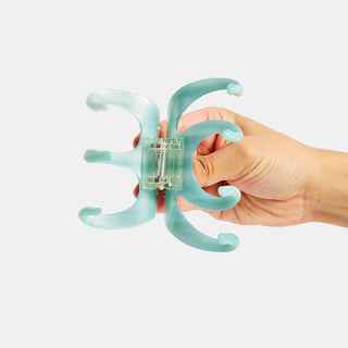 Hand holding a light blue claw clip opened against a white background