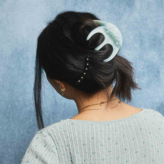 Person with a light blue hair clip in their hair against a blue background
