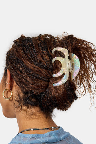 A close-up back view of a person with dark brown braided hair with a large translucent iridescent claw clip holding their hair up against a white background
