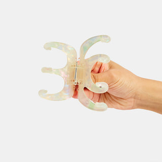 Hand holding a transparent, iridescent claw hair clip against a white background