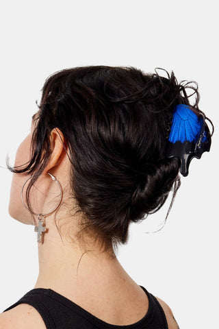 A close-up side view of a person with dark hair styled in an updo, wearing a bright blue and black hair claw clip