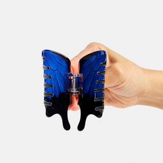 Hand holding a blue and black hair clip against a white background