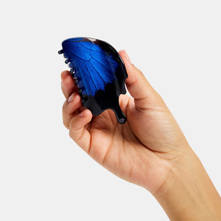 Hand holding a blue butterfly wing hair clip against a white background