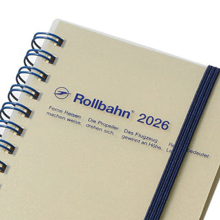 Beige notebook with blue spiral binding and 'Rollbahn 2026' branding on a white background