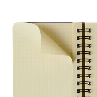 Close-up of a spiral-bound notebook with beige cover and grid interior pages. Shows perforation 
