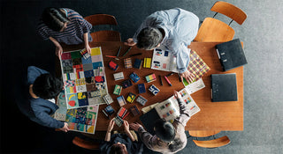 group of people standing around a large table with colorful posters and an assortment of notebooks with different covers on a table