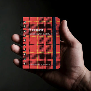 person holding pocket sized notebook with red, black, and yellow plaid design