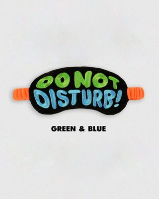 Sleep mask with 'Do Not Disturb!' text in green and blue on a white background