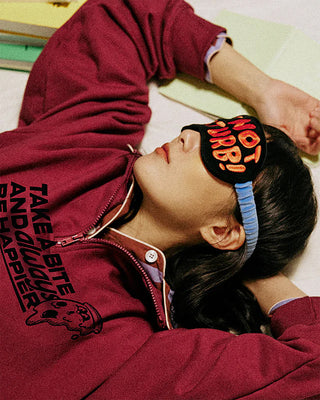 Person wearing a maroon hoodie with text and a sleep mask with 'Do Not Disturb!' 