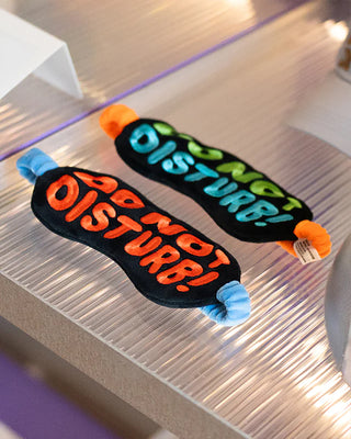 Two 'Do Not Disturb' eye masks on a reflective surface