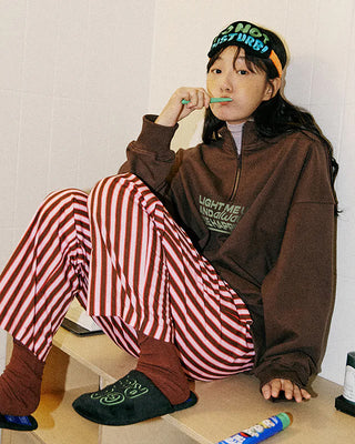 Person wearing a brown hoodie and red striped pants, brushing their teeth and wearing a sleep mask on their head.