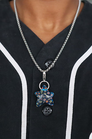 Close-up of a necklace with a blue floral pendant on a black shirt with white trim.