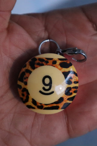 Pool ball keychain with number 9 and leopard print pattern held in a hand.
