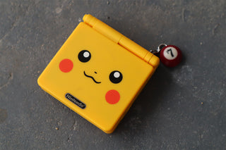 Yellow Pikachu Gameboy with a small burgundy pool ball keychain on a gray surface