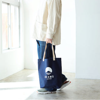 Person holding a blue tote bag with 'BEAMS JAPAN' logo in a bright room.