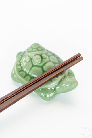 Green ceramic turtle-shaped chopstick rest with brown chopsticks on a white background