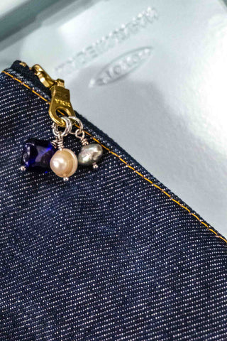 Close up of three pack charms on denim pencil case zipper with a blue background