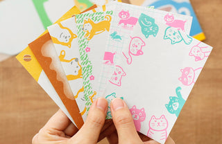 Hand holding colorful memo pad sheets with retro illustrations on a wooden surface