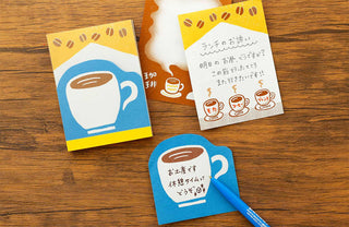 Three memo pad sheets with coffee-themed designs on a wooden surface.