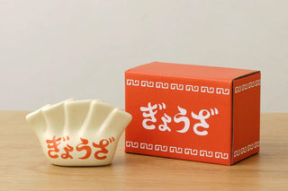 White porcelain pen holder with red text and a red box with white text on a wooden surface.