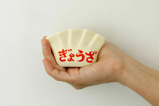 Hand holding a small white porcelain pen holder with red text on a plain background