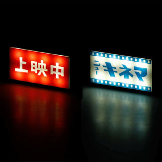 Two illuminated Japanese keychains on a black background, one glowing red with white characters and the other glowing white with blue characters and filmstrip borders.