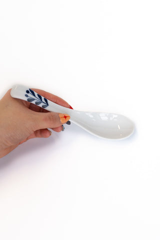 White spoon with blue design held by a hand on a white background