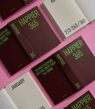 Collection of 'Happier 365' notebooks on a pink surface
