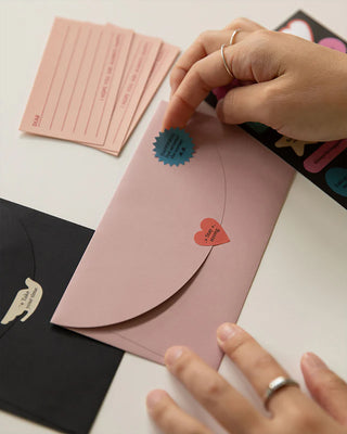 Person putting stickers on a pink envelope