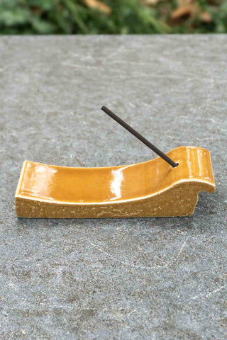 Terracotta ceramic incense holder with a single incense stick on a stone surface